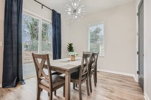 A dining area with a table and chairs, a chandelier, and a view through the window.