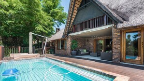 Un espace piscine agrémenté d’un pavillon à toit de chaume, de sièges extérieurs et d’une terrasse en bois.