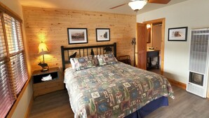 Un dormitorio con pared de madera, una cama con colcha, un ventilador de techo y una mesita de noche con lámpara.