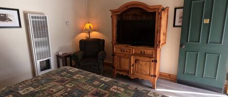 A bedroom with a bed, a wooden cabinet, a chair, a lamp, and a door.