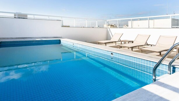 A rooftop pool with clear blue water, surrounded by lounge chairs and a white railing. - Studio Moderno Bela Vista | Wifi 250 mb (São Paulo)