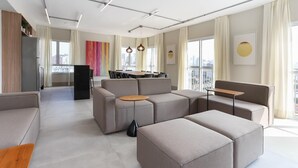 A modern living room with a sofa, ottoman, and a dining area in the background. - Studio Moderno Bela Vista | Wifi 250 mb (São Paulo)