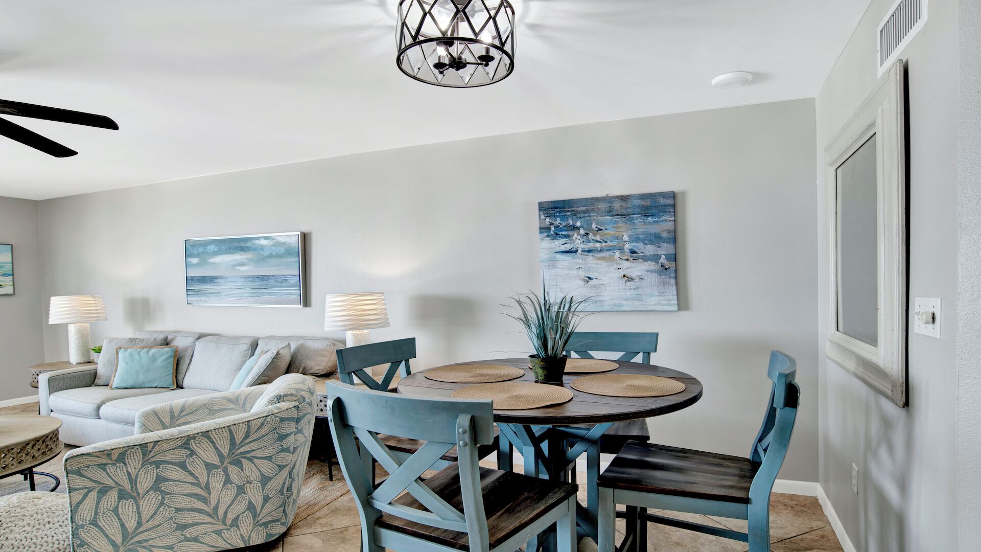 Un coin repas avec une table ronde, des chaises bleues et un ventilateur de plafond.