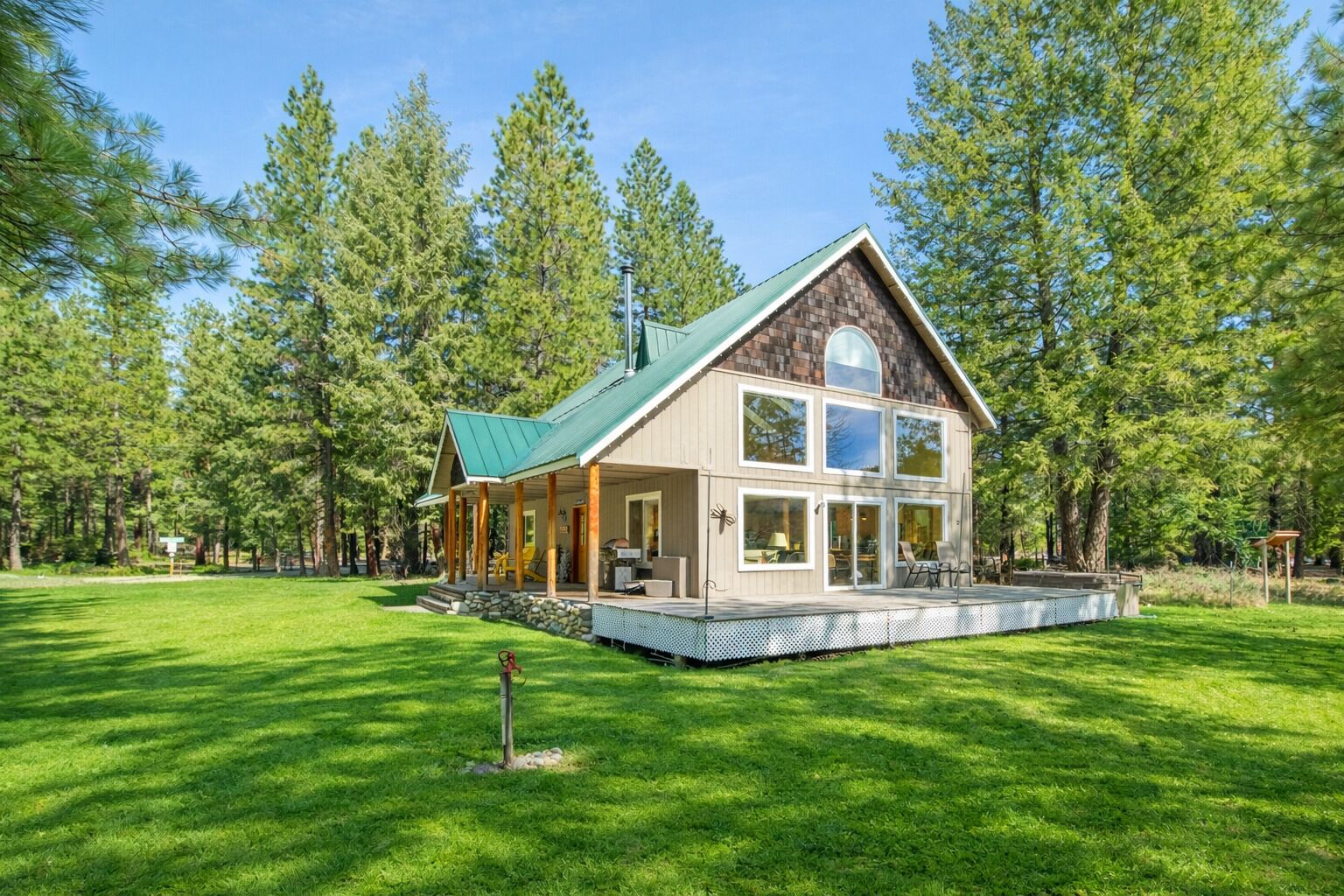 A two-story cabin with a green roof, large windows, and a deck.