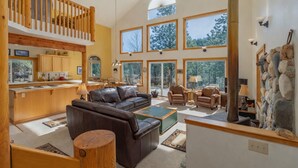 A spacious living area with a high ceiling, large windows, a wooden staircase, and a stone wall.
