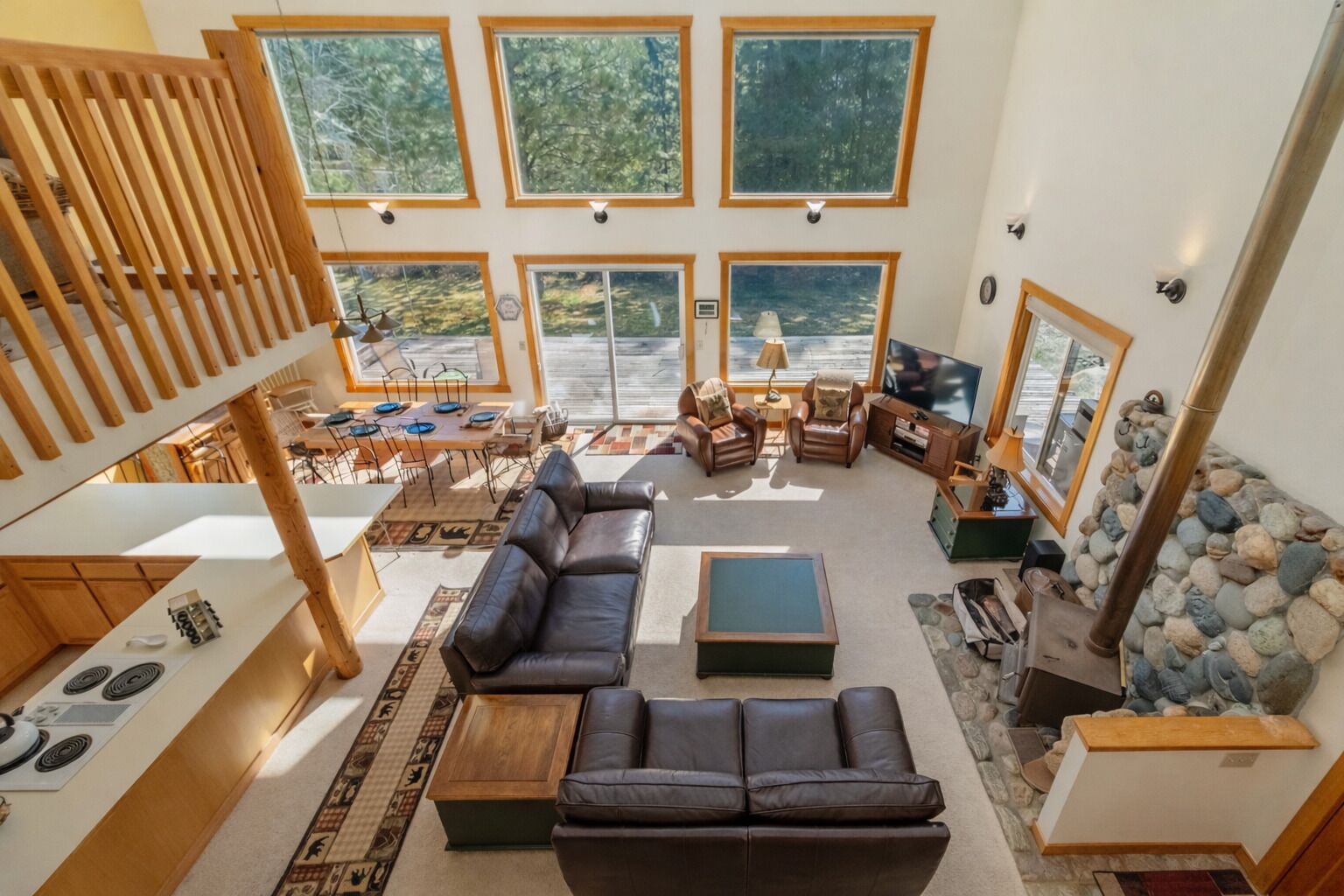 A spacious living area with a large sofa, a coffee table, and a fireplace. There are multiple windows providing natural light and views of the outdoors.