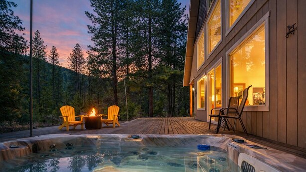 A hot tub with two chairs and a fire pit, surrounded by a deck and forest.