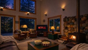 A cozy living room with a stone fireplace, leather sofas, a coffee table with popcorn, and a TV displaying 'NETFLIX'.