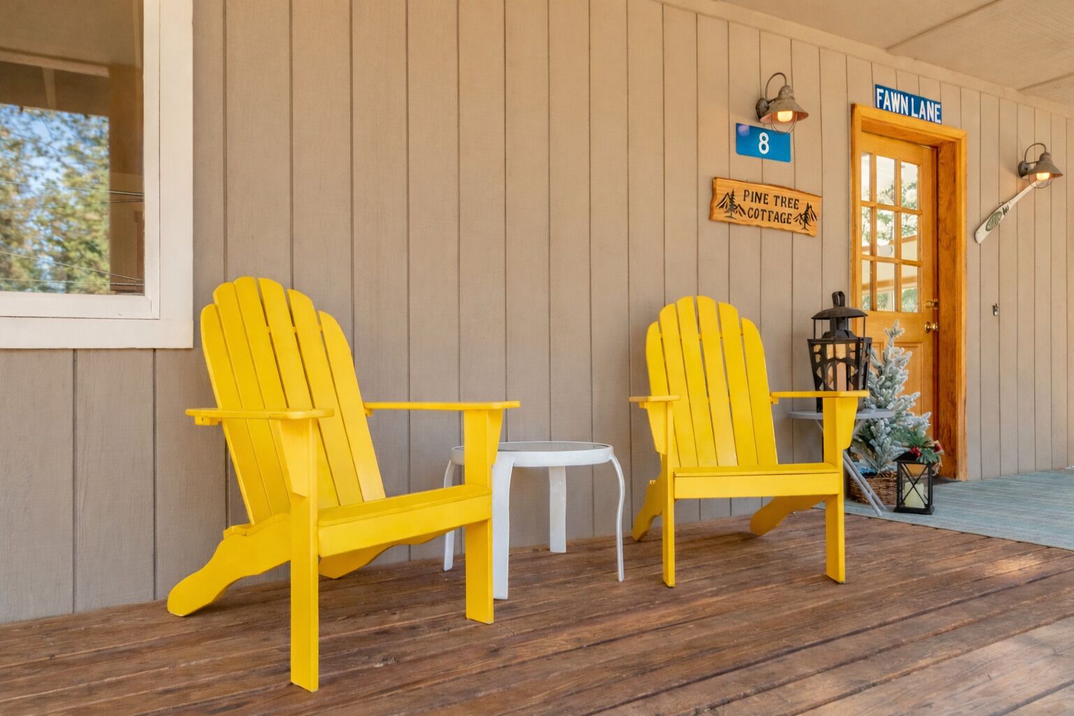 A porch with two yellow Adirondack chairs, a small white table, and a door labeled "Fawn Lane".