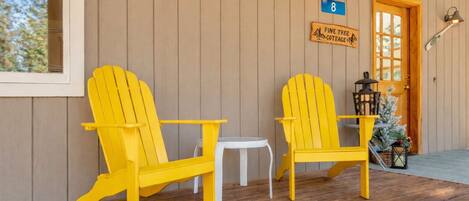 A porch with two yellow Adirondack chairs, a small white table, and a door labeled "Fawn Lane".