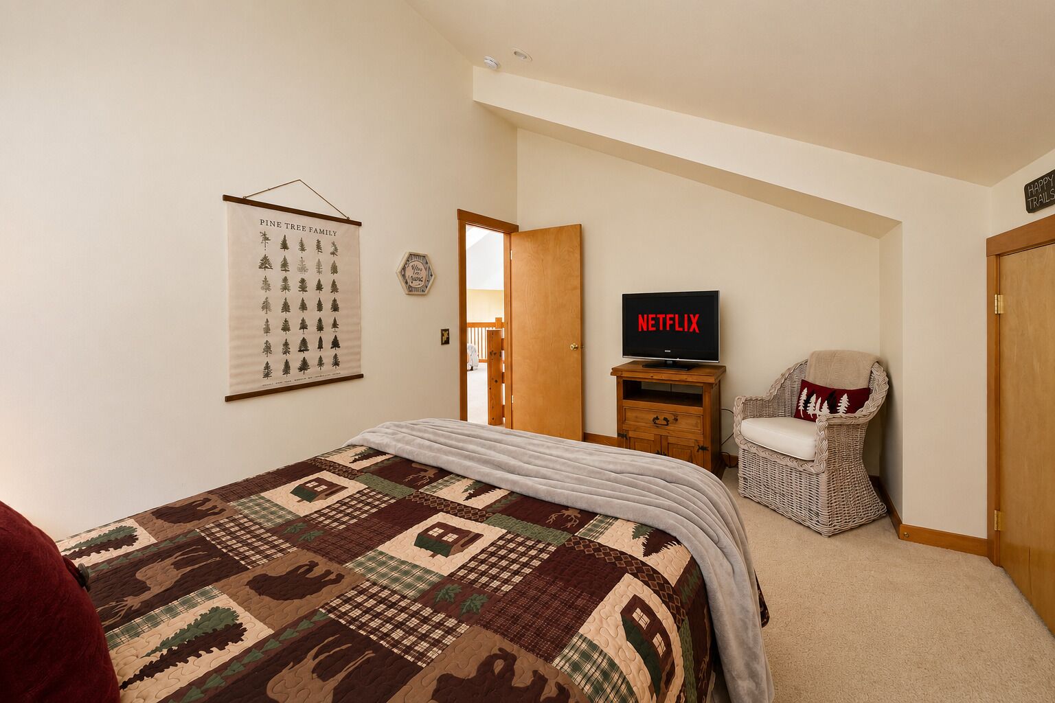 A bedroom with a bed, a television, a wicker chair, and a door leading to another room.