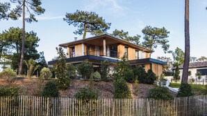 A modern two-story house with a wooden exterior, a balcony on the upper floor, and a landscaped garden with various shrubs and trees. - SPRING . KEYWEEK - Contemporary villa with pool in the hea (Anglet)