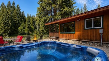 A hot tub with a wooden deck, surrounded by a forest, and a building with large windows.