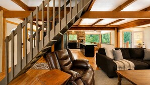 A spacious living area with a wooden staircase, leather furniture, and a view of the outdoors.