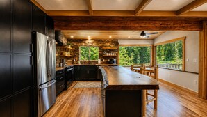 A modern kitchen with a central island, wooden beams, stone accents, and large windows.