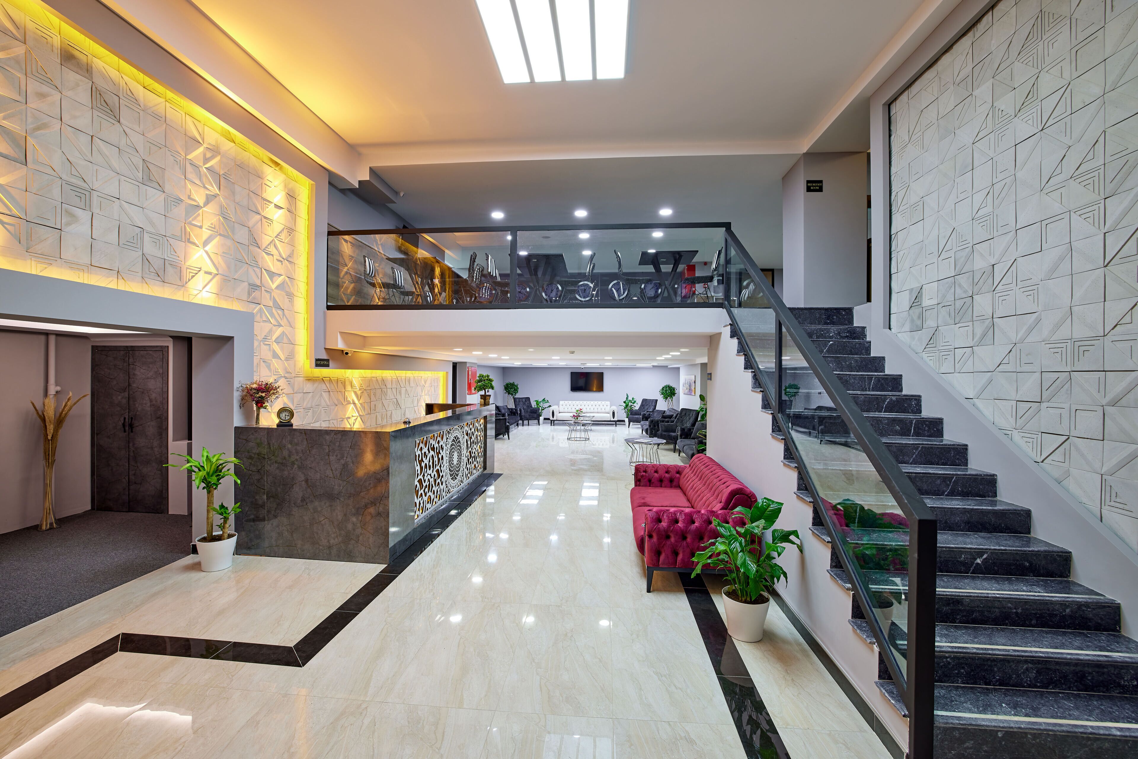 A spacious lobby with a marble floor, a reception desk, a staircase, and seating areas.