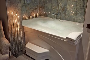 A modern bathroom with a large bathtub, marble walls, and candles. - The Bold Hotel (Istanbul)