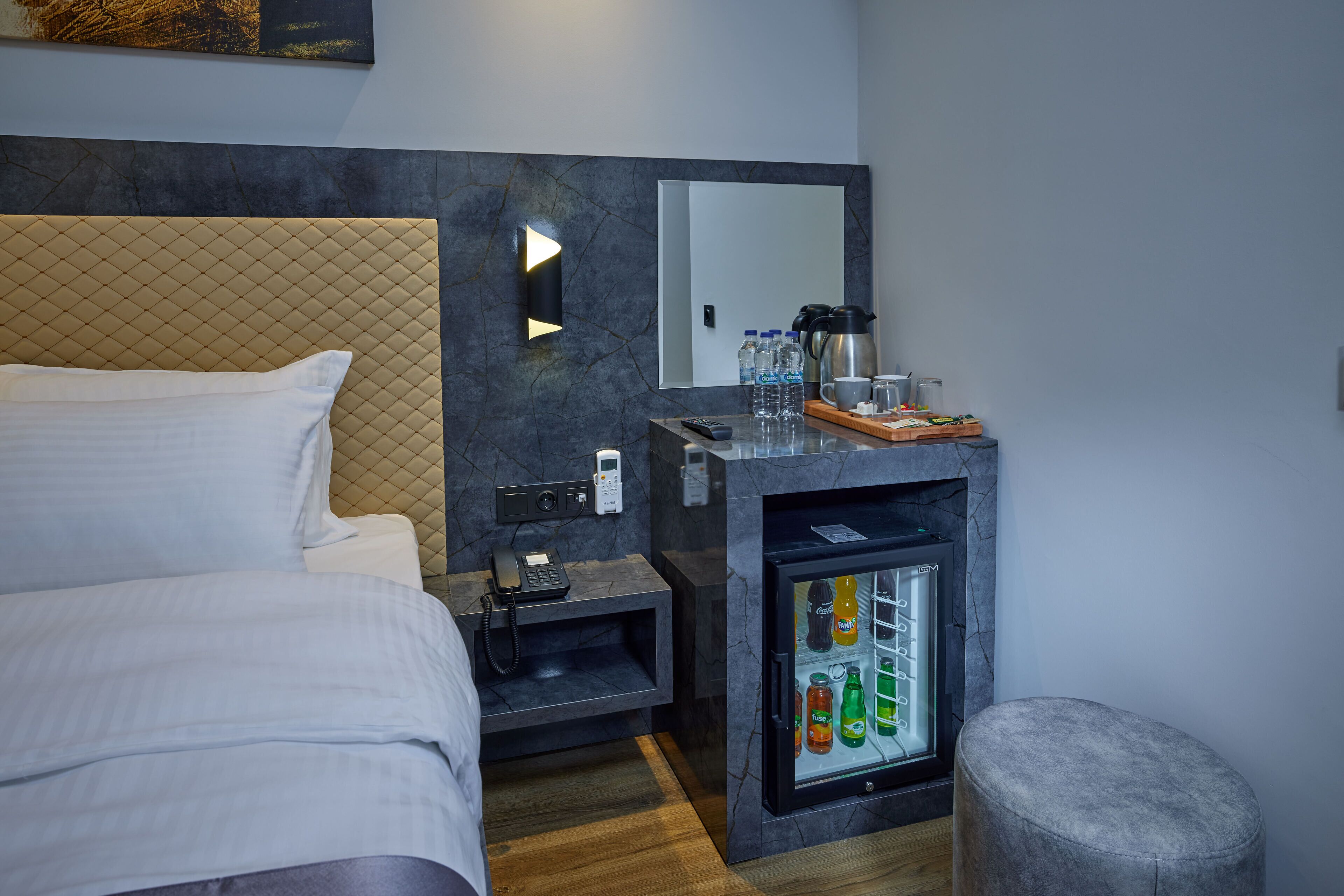 A modern hotel room with a bed, a minibar, a coffee maker, and a mirror.