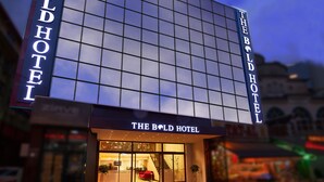 Um hotel com uma grande fachada de vidro e sinalização iluminada com a inscrição "The Bold Hotel".