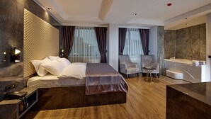 Quarto de hotel moderno com uma cama grande, área de estar, banheira e toucador.
