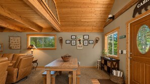 A cozy cabin interior with a wooden ceiling, a dining table, a sofa, and a door labeled 'CABIN'. - Lil Bigfoot Chalet 2 Bedroom Home by NW Comfy Cabins by RedAwning (Leavenworth)