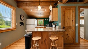 A kitchen with wooden cabinets, a central island with stools, a refrigerator, and a clock on the wall. - Lil Bigfoot Chalet 2 Bedroom Home by NW Comfy Cabins by RedAwning (Leavenworth)