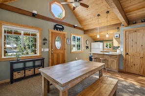 A cabin interior with a wooden dining table, a kitchen with a sink, and a ceiling fan.