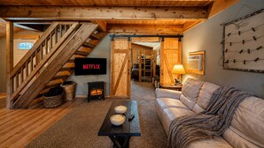 A cozy living room with a fireplace, a sofa, a coffee table, and a TV displaying 'NETFLIX'. - Lil Bigfoot Chalet 2 Bedroom Home by NW Comfy Cabins by RedAwning (Leavenworth)