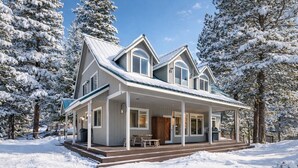 Una casa a due piani con un portico coperto, circondata da alberi innevati.