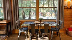 Ein Essbereich mit Tisch und Stühlen, ein Fenster mit Blick auf Bäume und eine Wandlampe.