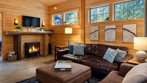 Ein gemütliches Blockhaus-Interieur mit Kamin, Ledersofa und großen Fenstern mit Blick auf den Wald.