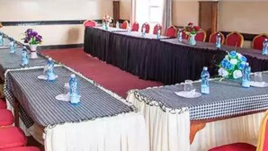 Un salón de conferencias con largas mesas, sillas rojas y botellas de agua.