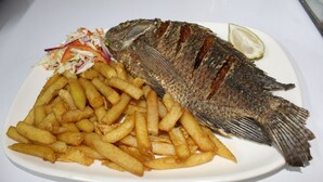 Un plato con un pescado entero, papas fritas y una ensalada.