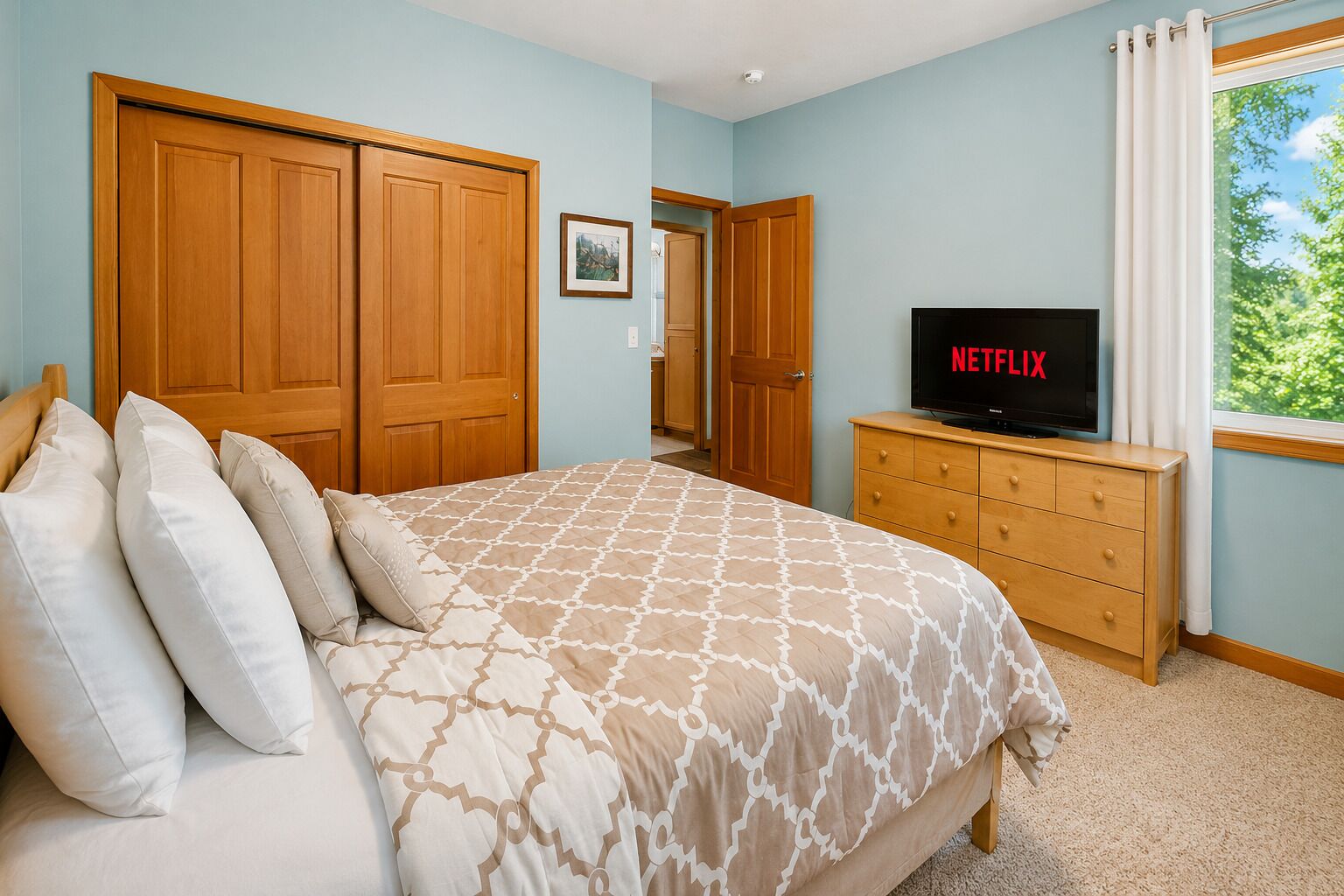Une chambre à coucher avec un lit, une armoire en bois, un téléviseur posé sur une commode et une fenêtre avec des rideaux.