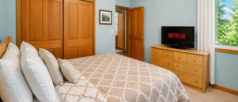 Une chambre à coucher avec un lit, une armoire en bois, un téléviseur posé sur une commode et une fenêtre avec des rideaux.
