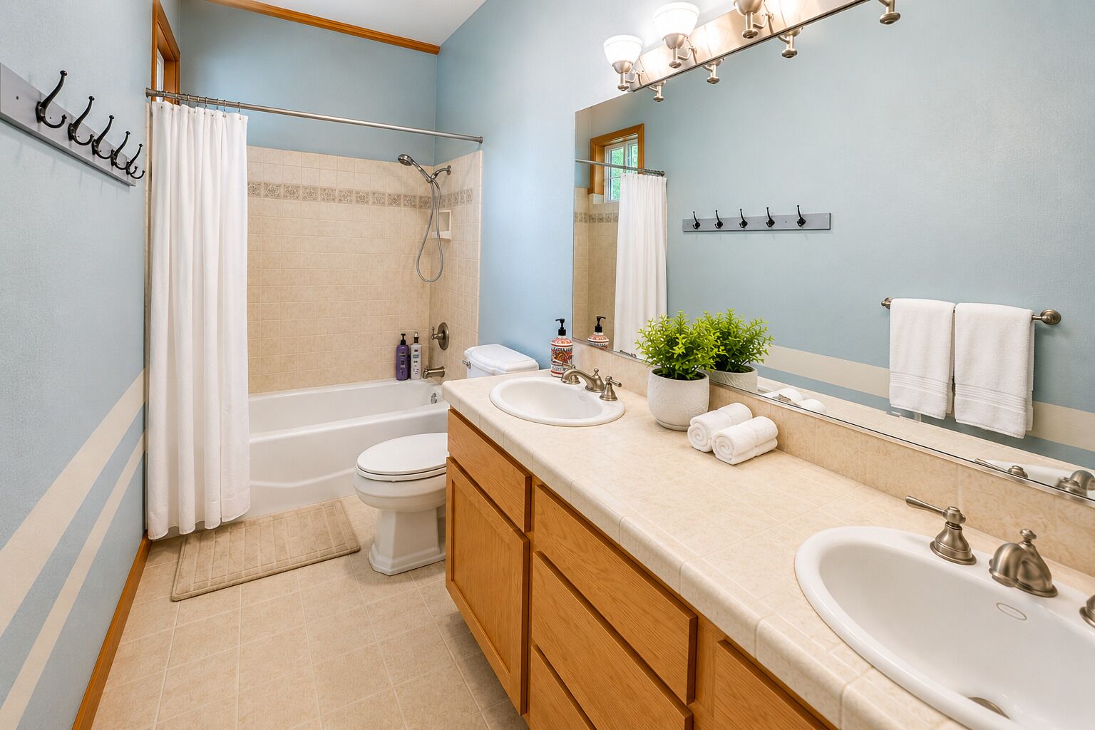 A bathroom with a bathtub, toilet, two sinks, a mirror, and a potted plant.