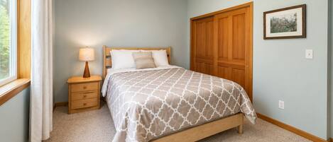 A bedroom with a bed, nightstand, lamp, wooden wardrobe, and a framed picture on the wall.