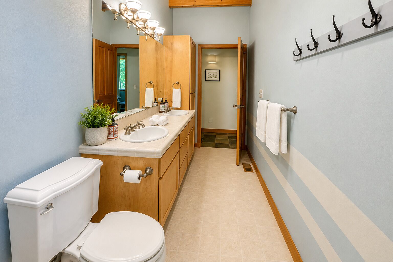 A bathroom with a toilet, sink, and mirror. There is a plant on the sink counter, and towels are hung on a rack.