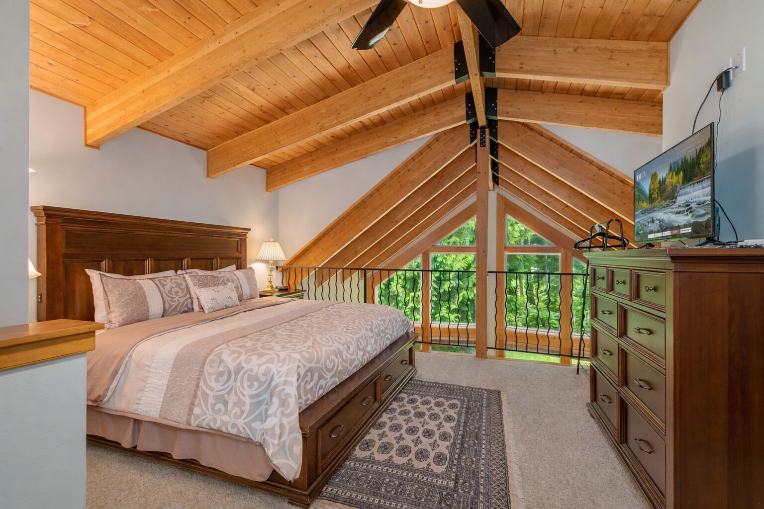A bedroom with a sloped ceiling, a bed with patterned bedding, a dresser, and a television on a stand.