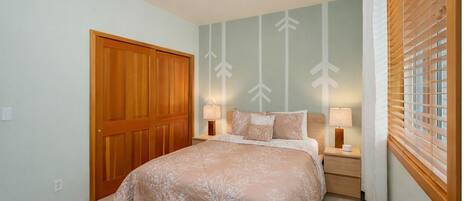 A bedroom with a large bed, two bedside tables, a wooden wardrobe, and a window with blinds.