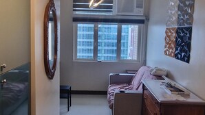 A bedroom with a bed, a dresser, a mirror, and a window with a view of buildings.