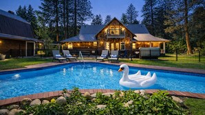 A pool with a swan float, surrounded by a stone patio and greenery. - Family Cabin 5 Bedroom Home by NW Comfy Cabins (Leavenworth)