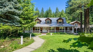A two-story wooden house with a porch, surrounded by trees and a well-maintained lawn. - Family Cabin 5 Bedroom Home by NW Comfy Cabins (Leavenworth)