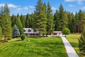 A two-story lodge with a covered porch, surrounded by a well-maintained lawn and dense forest. - Family Cabin 5 Bedroom Home by NW Comfy Cabins (Leavenworth)