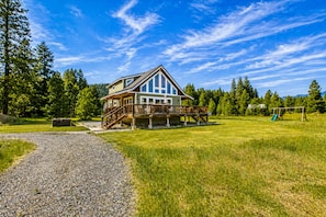 A two-story house with a deck, surrounded by a grassy yard and trees. - Peterson Acres 3 Bedroom Home by NW Comfy Cabins by RedAwning (Leavenworth)