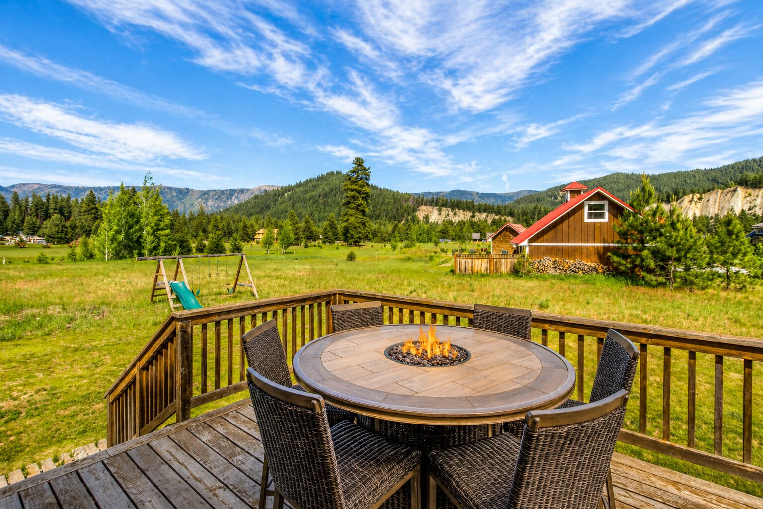 A wooden deck with a round table and chairs, a fire pit, and a swing set.