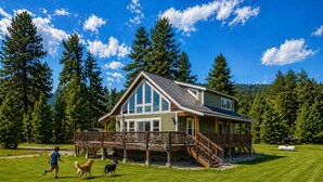 A two-story lodge with a deck, surrounded by a forest.