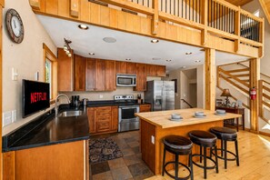A modern kitchen with wooden cabinets, stainless steel appliances, a central island with stools, and a visible Netflix sign. - Peterson Acres 3 Bedroom Home by NW Comfy Cabins by RedAwning (Leavenworth)