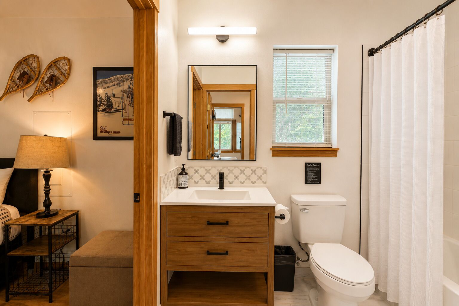 Une salle de bain avec un meuble-lavabo en bois, des toilettes, une fenêtre avec des stores et un miroir.