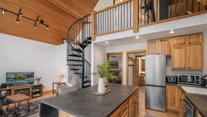 A modern kitchen with wooden cabinets, a central island, and a spiral staircase. - Raven Haven Lodge 2 Bedroom Home by RedAwning (Leavenworth)